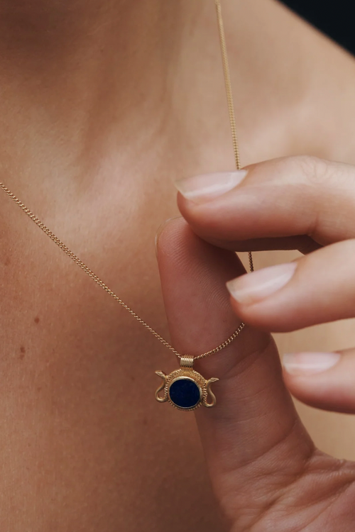 Gold necklace with a blue pendant being worn on a person's neck.