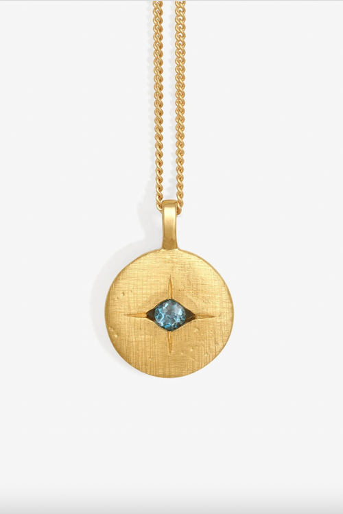 Gold necklace with a round pendant featuring a blue gemstone on a white background