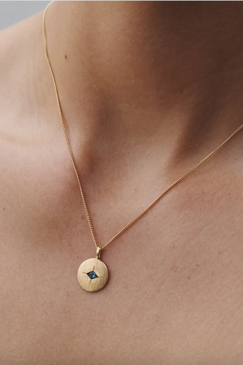 Gold necklace with a round pendant featuring a blue gemstone on a person's neck.